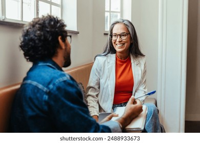 Two coworkers engaging in a creative conversation while seated in an office lounge area, fostering a collaborative work environment.