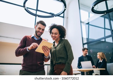 Two Coworkers Standing In An Office, Holding A Digital Tablet