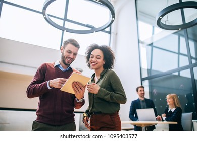 Two Coworkers Standing In An Office, Holding A Digital Tablet