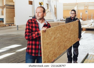 Two co-workers in a woodworking factory carrying a large sheet of chipboard ready to use in the manufacturing of prefabricated products - Shutterstock ID 2111628797