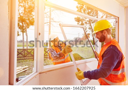 Two craftsmen from a glazier assemble windows in the new house