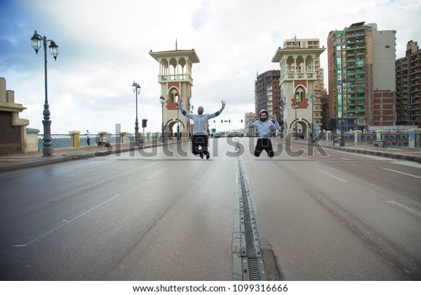 Two crazy friends standing in the middle of an empty\
street and jumping up