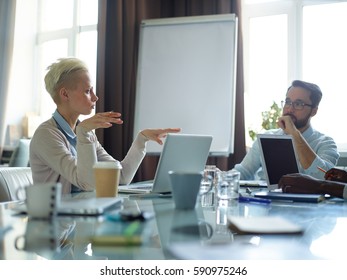 Two Creative Business People Dressed In Casual Clothes Having Long Discussion Over Work Related Issues And Sitting At Messy Meeting Table In Modern Conference Room