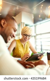 Two Creative Millenial Small Business Owners Working On Social Media Strategy Using A Digital Tablet While Sitting At Desk