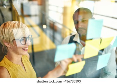 Two creative millenial small business owners working on social media strategy brainstorming using adhesive notes in windows - Powered by Shutterstock