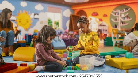 Two Creative Multiethnic Girlfriends Playing in Kindergarten. Little Indian and African Girls Constructing a House Out of Colorful Building Blocks. Children Having Fun in Modern Daycare Center