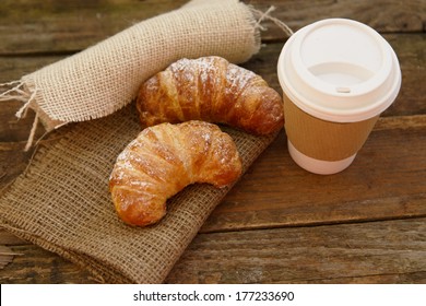 Two croissants and coffee-to-go in a rustic setting
