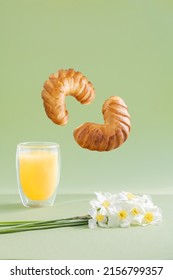 Two croissants flying on light green background with orange juice and white daffodils flowers