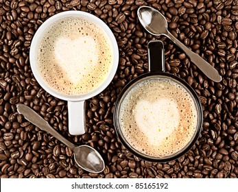 Two cups with Cafee Latte with heart shaped rosetta surrounded by coffee beans and spoons