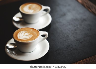 Two cups of cappuccino with latte art on black table. Morning coffee for couple in love. Top view. - Powered by Shutterstock