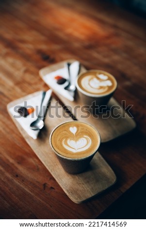 Two cups of cappuccino with latte art on wooden background. Beautiful foam, heart shaped coockies, top view.