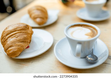 Two cups of capuccino coffee with croissants on a wooden table. Having morning coffee in outdoor cafe.