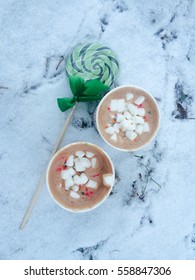 two cups of cocoa with candy on the snow