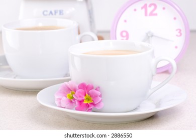Two cups of coffee (could be a cocoa) and a clock.