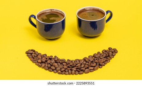 two cups of coffee and an emoticon made of coffee beans on a yellow background, place for text and copy space. - Shutterstock ID 2225893551