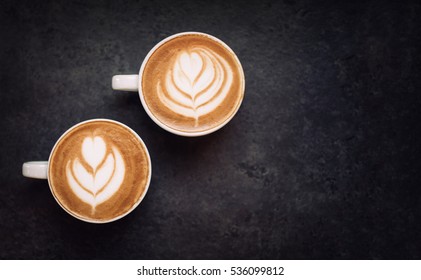 Two cups of coffee on black rustic background with beautiful latte art