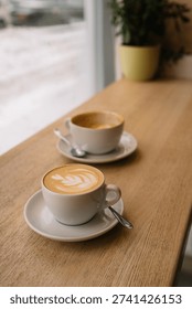 Two cups of coffee on window bar table with snow outside