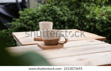 Two cups of coffee and tea on a wooden table, green trees around 