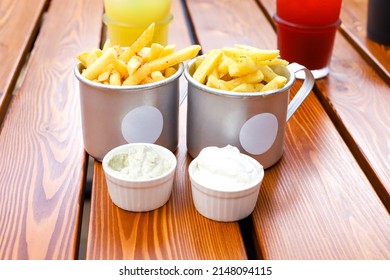 Two cups of french fries and two creamy sauces, lemonades on brown boards wooden table. Fastfood, potato. Front view, mockup.