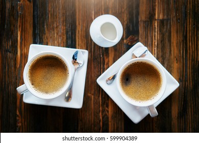 Two Cups Of Fresh Coffee On Wooden Table With Creamer From Top Down View