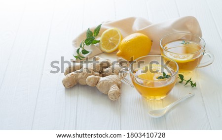 Two cups of healthy ginger tea with mint leaves and lemon on white table. Space for your text