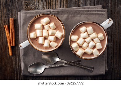 Two Cups Of Hot Cocoa With Marshmallows And Cinnamon Sticks On Wooden Background