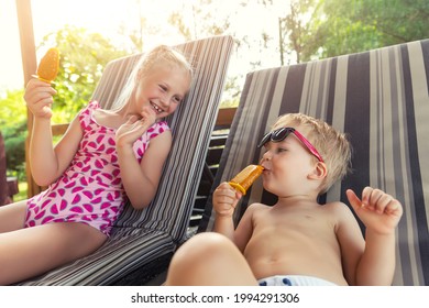 Two cute adorable caucasian blond little siblings enjoy having fun relaxing and eat fruit popsicle icecream sitting on sunbed in yard garden near pool sea beach. Brother and sister chilling outdoor - Powered by Shutterstock