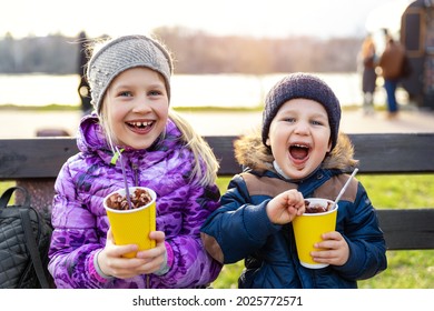 Two cute adorable siblings children sitting on bench drink delicious yummy hot chocolate, tea cocoa from paper cups during walk at city street park or backyard outdoors. Brother and sister enjoy fun - Powered by Shutterstock