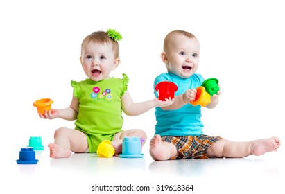 Two Cute Babies Playing With Color Toys. Children Girl And Boy Sitting On Floor. Isolated On White Background.