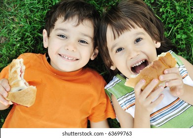 Two cute boys laying on ground in nature and happily eating healthy food - Powered by Shutterstock