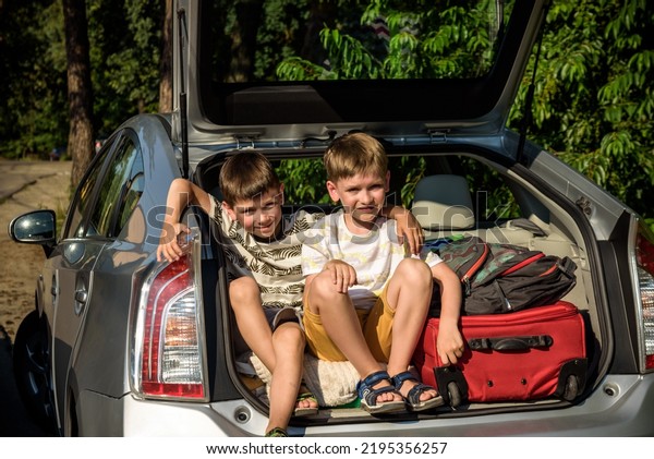 Two cute\
boys sitting in a car trunk before going on vacations with their\
parents. Two kids looking forward for a road trip or travel. Summer\
break at school. Family travel by\
car.