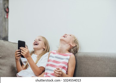 Two Cute Caucasian Blonde Girls Sisters Holding Cell Phone And Laughing.