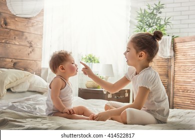 Two Cute Child Baby Girls Playing And Having Fun On The Bed. Loving Sisters Hug