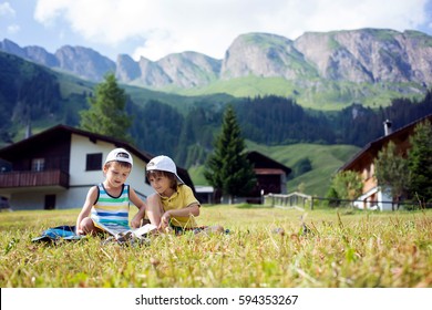 Two cute children, reading a book on a lawn in Swiss alps, summertime