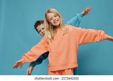 two cute children of school age in multi-colored sweaters stand on a blue background, a boy and a girl stand with their hands apart, depicting airplanes. The theme of friendship between children