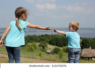 Two cute children, sister and brother, reaching towards each other by hands over beautiful landscape, help and support concept, friend and family, summer outdoor