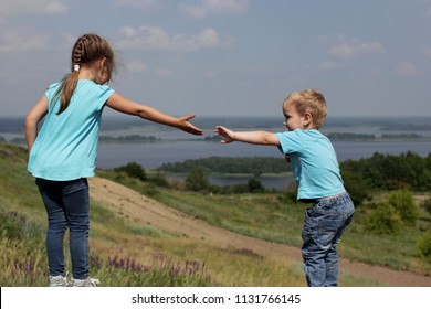 Two cute children, sister and brother, reaching towards each other by hands over beautiful landscape, help and support concept, friend and family, summer outdoor