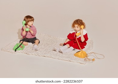 Two cute children, sister and brother sitting on floor and playing together isolated over grey background. Concept of happy childhood, leisure activities, fun, lifestyle, family, retro style