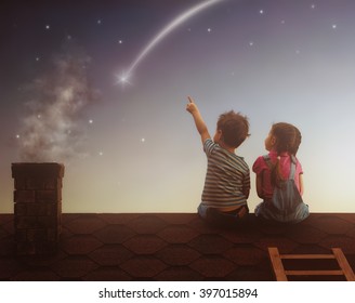 Two cute children sit on the roof and look at the stars. Boy and girl make a wish by seeing a shooting star.