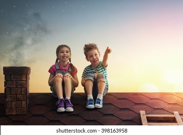 Two cute children sit on the roof and look at the stars. Boy and girl make a wish by seeing a shooting star.