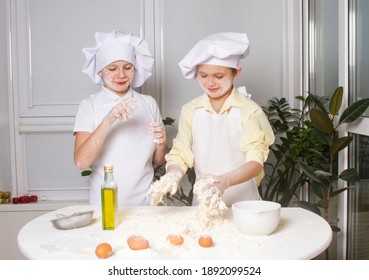 Two cute European boys dressed as a cook are kneading flour, milk and eggs, children are playing in the kitchen, teenagers are making a pie from the dough.
