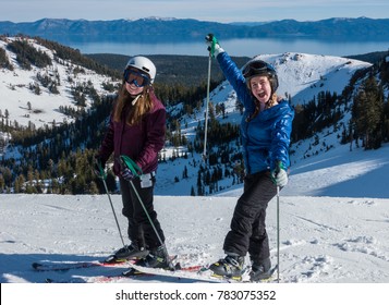 Two Cute Girls At The Top Of The Ski Run At Alpine Meadows Ski Resort, Part Of Squaw Valley Resort, In The Sierra Nevada Mountain Range Of California, With A View Of Lake Tahoe In The Background.  