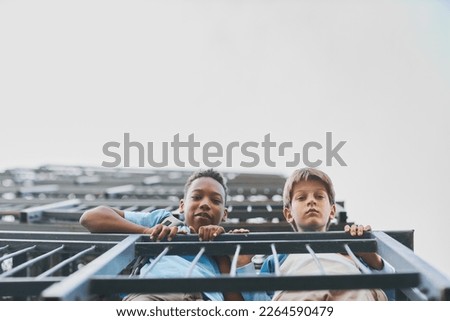 Two cute intercultural youngsters peeking out of balcony of skyscraper while holding by metallic railings and looking at camera