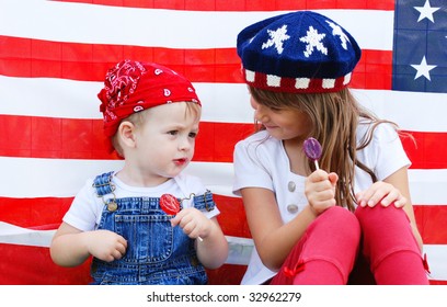 Two cute kids eating suckers by an american flag