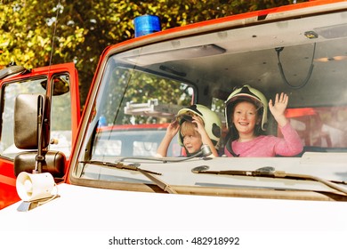  Two Cute Kids Playing In Fire Truck, Pretending To Be Firefighters, Open Doors Day At Fire Station. Future Profession For Children. Educational Program For Schoolkids 