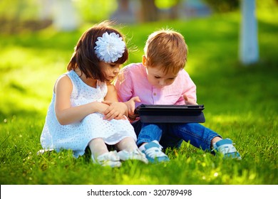 Two Cute Kids Using Digital Tablet In Summer Garden