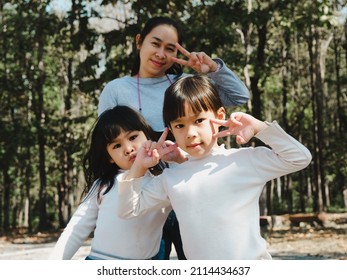 Two cute little Asian girls in summer outfits, having fun with a beautiful young mother smiling happily in the park. Motherhood and family concept.	