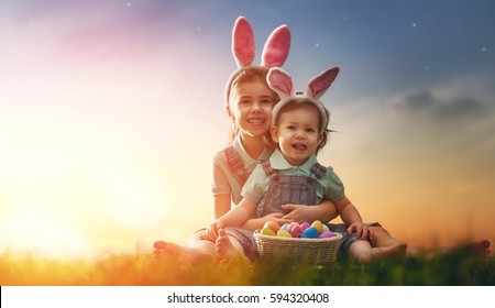 Two cute little children wearing bunny ears. Girls are sitting on the lawn. Kids with Easter eggs in the rays of the setting sun. - Powered by Shutterstock