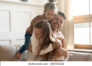 Two cute little daughters cuddling loving father congratulate him Happy Father Day sit on sofa having fun on weekend playing active games laughing feels overjoyed. Family bonds, love, devotion concept - Powered by Shutterstock