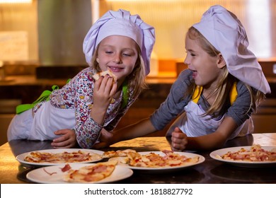 Two Cute Little Girls In Chef Hats Eating Pizza After Cooking Master Class